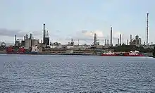 Photo de bateaux situés sur la mer face à un complexe industriel incluant une raffinerie de pétrole.