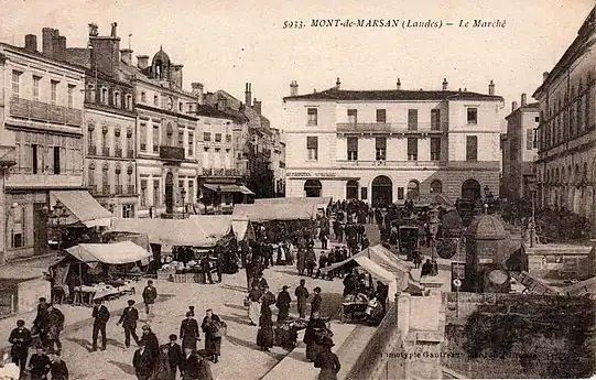 Photo ancienne de la place, un jour de marché. La place est bordée côté est par le théâtre, côté nord par la maison Du Lyon (actuelle Société Générale), et côté ouest par l'ancien hôtel de ville