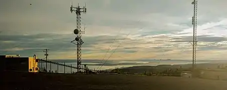 Des tours de télécommunication avec un estuaire et des collines au coucher du soleil.