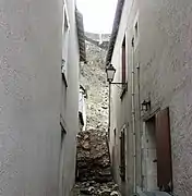 Photographie d'un bloc de maçonnerie encastré entre deux maisons dans une ruelle.