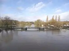 photographie en couleurs d'un cours d'eau dont le niveau attend la base d'une passerelle et qui noie les rives.