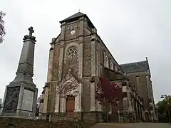 Photographie en couleurs de la façade d'une église avec un monument aux morts au premier plan.
