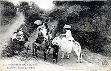 Photo en noir et blanc, femmes en robes longues et chapeau, juchées en amazone sur des ânes.