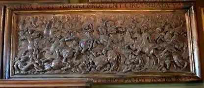 Vue d'un panneau de bois sculpté représentant une scène de guerre.