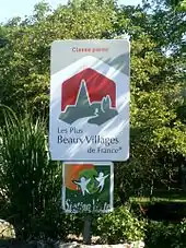 Panneau en couleurs représentant un village stylisé avec légende « classé parmi les plus beaux villages de France ».