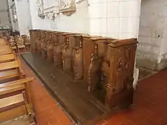 Vue de sept stalles en bois alignées contre le mur intérieur d'une église.