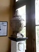 Vue d'une urne funéraire en forme de vase posée sur un piédestal près d'une fenêtre.