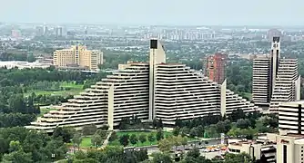 Une grande pyramide vue presque de face et une autre vue de profil au milieu du parc olympique. En fond, on voit le reste de la ville de Montréal.