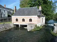 Photographie en couleurs d'un bâtiment dont la façade présente des lits alternés de pierre et de briques construit au dessus d'un cours d'eau.