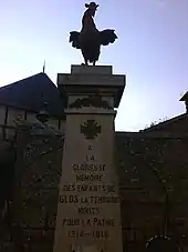 Photographie d'une colonne carrée surmontée de la statue d'un coq