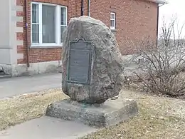 Photographie en couleur d'un monument prenant la forme d'une imposante pierre sur laquelle est fixée une plaque commémorative.