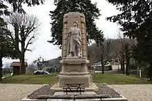 Le monument aux morts est un obélisque décapité, taillé sur les sommets. Il est entouré d'arbres et de buissons tous verts. De sa face avant sort un poilu de la Grande guerre.