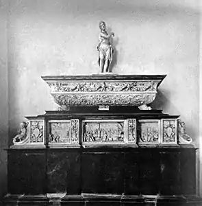 Photographie en noir et blanc d'un sarcophage surmonté d'une statue et posé sur un piédestal.