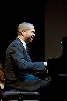 Photo couleur d'un homme en costume, souriant, assis au piano