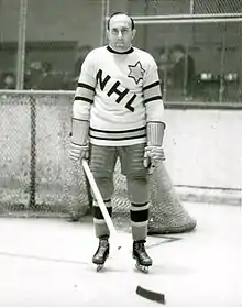Photo de Morenz devant un but dans un chandail blanc marqué des lettres NHL.