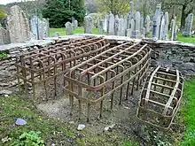 Photographie de trois cages de forme rectangulaires sans fond exposées dans un cimetière.