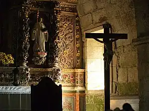 Crucifix situé devant une fenêtre latérale et un retable baroque.