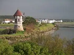 Photographie montrant la rive d'un cours d'eau visible à droite, surmontée d'un petit moulin sur la droite.