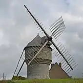Vue d'un moulin aux ailes déployées sans voile, au toit d'ardoise, sur fond de ciel nuageux.