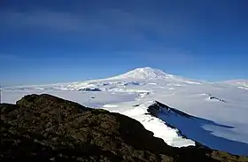 Relief volcanique entièrement couvert de neige vu depuis une péninsule rocheuse distante.