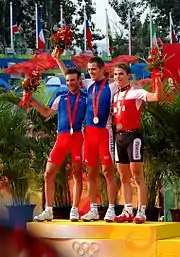  Trois coureurs cyclistes debout sur un podium portant une médaille autour du cou et tenant un bouquet de fleurs.