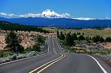 Le mont Jefferson vu au loin dans l'axe d'une route rectiligne traversant une plaine.