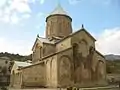 Monastère en forme de temple en croix avec arcatures en pierre de couleur sable et surplombé par un clocher surmonté d'une croix orthodoxe.