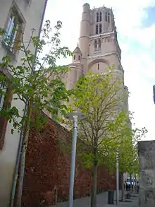 Photo couleur d'un mur ancien de briques rouges bordant une ruelle. En arrière-plan, le clocher de la cathédrale indique la situation dans la cité épiscopale.