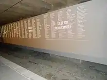 Image d'un mur gris en diagonale gravé de noms sous une toiture.