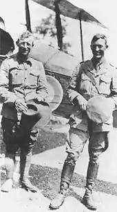 Photo en noir et blanc représentant deux hommes debouts, souriants en tenues militaires.