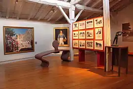 Vue de l’intérieur d’un musée, avec statues, tableau sur un mur et panneau de photographies.