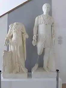 Vue d'un groupe de deux statues dont l'une, une femme, n'a pas de tête et l'autre, un homme, porte une cruche et une sorte de bâton.