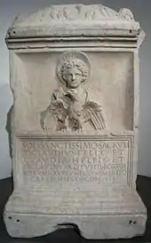 pierre blanche rectangulaire portant sur la moitié supérieure le buste d'un homme auréolé d'un soleil avec un aigle devant lui, dans la partie inférieure une inscription latine.