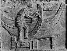 Bas-relief. En arrière-plan une coque terminée, au premier plan homme de profil debout maniant une herminette.