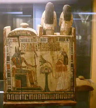 photographie d'un coffret décoré par une image d'Anubis assis sur un trône.