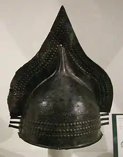 Dans un musée, casque en bronze pointu sur le dessus.