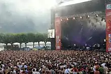 Photographie en couleurs d'une scène et du public d'un concert en plein air.