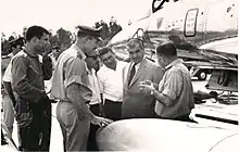 Groupe d'hommes debout, en uniforme ou en costume sur une base aérienne