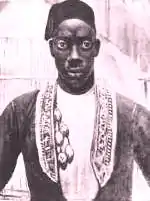 Photo noir et blanc d'un homme noir, de face, en vêtement à parures