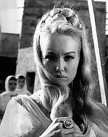 Photogramme en noir et blanc cadré sur une belle jeune femme blonde, dans un costume antique, regardant l'objectif.