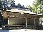 Un bâtiment en bois avec plancher légèrement surélevé, un toit en croupe et à pignon et un auvent au-dessus des marches.