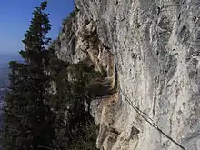 Chemin taillé à flanc de falaise avec un câble pour s'assurer.