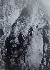 Photographie ancienne avec trois hommes sur le point de franchir une passerelle.