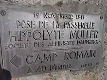 Plaque en métal sombre scellée dans la roche avec les commentaires : « 19 novembre 1911 - Pose de la passerelle Hyppolyte Müller - Société des alpinistes dauphinois - Camp romain à 40 minutes »