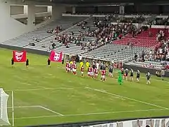 Photographie en couleur d'un terrain de football où deux équipes font leur entrée.