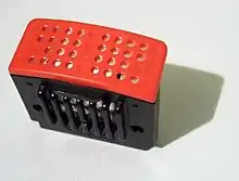 Petite boite noire, avec un couvercle perforé de couleur rouge.