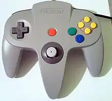 Manette de jeu grise avec une croix directionnelle, un stick analogique et une dizaine de boutons colorés.