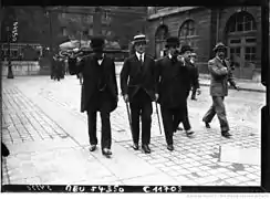 Trois hommes marchent et l'un d'eux se cache du photographe grâce à son parapluie.