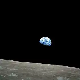 Le sol lunaire est visible en bas de l'image et la Terre au centre.