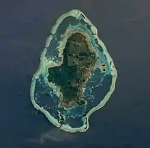 Photographie satellite d'une île en forme ovale, entourée d'eau (lagon) délimité par une bande plus claire (le récif)